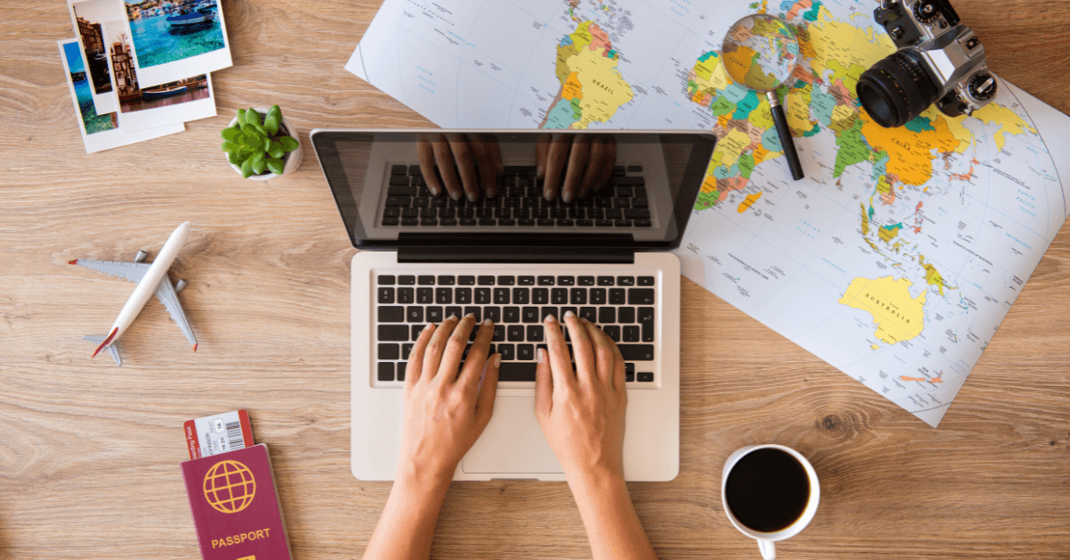 Woman planning solo travel with a laptop, passport, coffee, and world map spread out on a table.