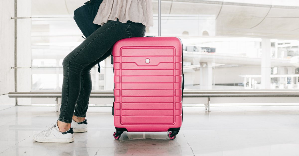 A woman sitting on her suitcase at the airport showing minimalist packing in action with no extra baggage required.