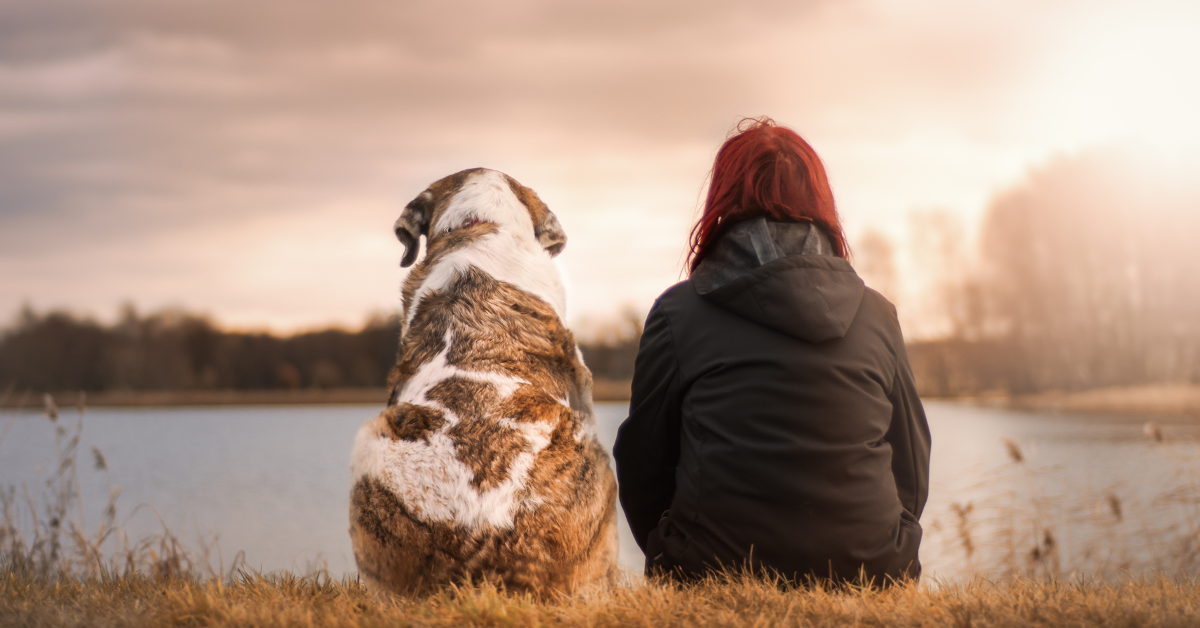 A woman and her dog sitting in nature by a quiet lake, showing stress-relief secrets for women 40+ through a simple moment of calm.