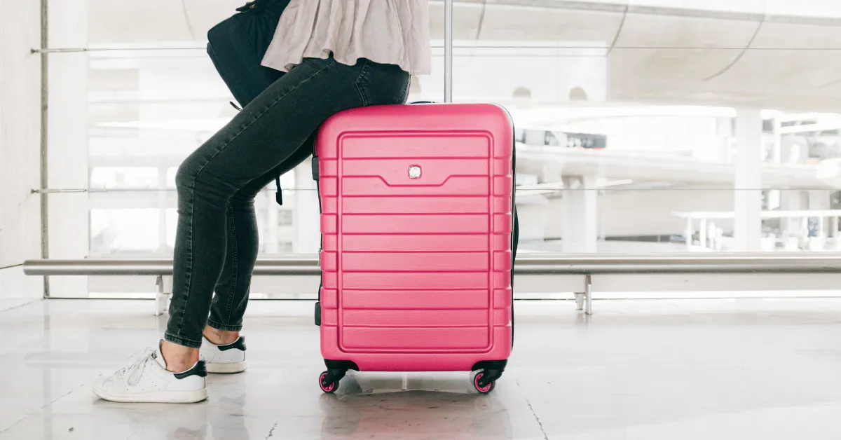 A woman sitting on her suitcase at the airport showing minimalist packing in action with no extra baggage required.