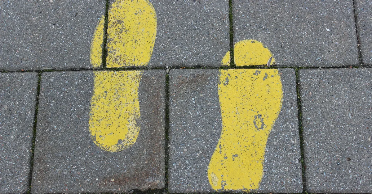 A top-down view of two painted yellow footprints on a gray concrete walkway, symbolizing the first steps in a midlife routine for midlife fitness for women.