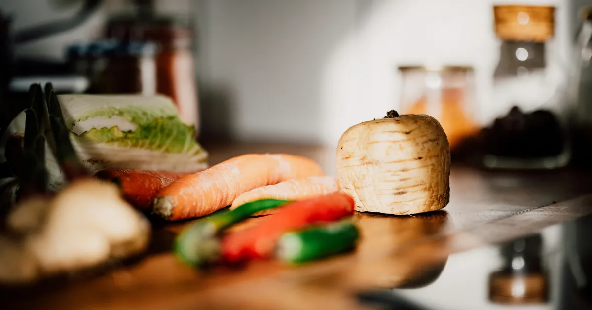 Cabbage, carrots, green chilis, and a turnip on a wooden countertop, a visual of simple eating habits for women over 40.