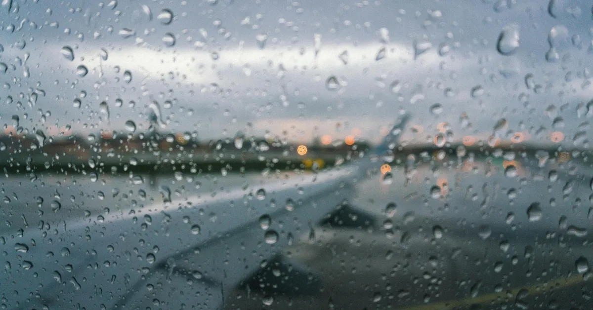 Rain on an airplane window looking out over the runway, showing what staying healthy while traveling feels like when the body slows down between destinations.